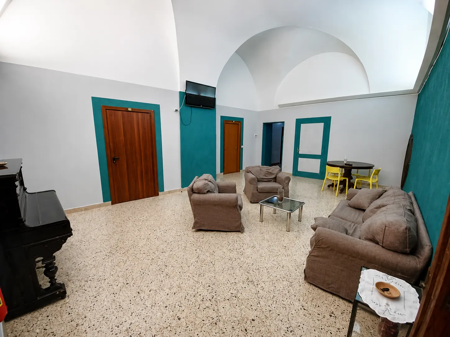 Sala comune di Domus Narnia con divani, pianoforte e volte originali del convento